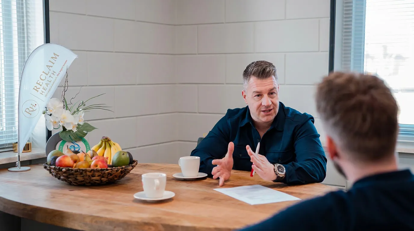 Arnold in gesprek aan tafel, met de banner van Reclaim Health naast hem